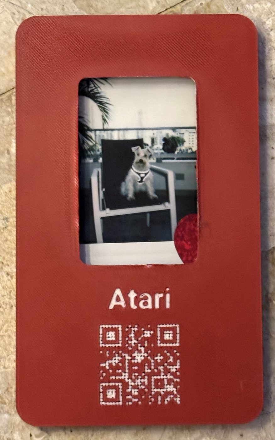 Placa impresa en 3D, roja, con una foto Instax de Atari, un schnauzer sentado en una silla; debajo, el nombre «Atari» y un código QR grabados hasta el blanco